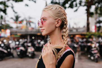 Pensive blonde woman in black attire posing on blur street background. Outdoor shot of serious...