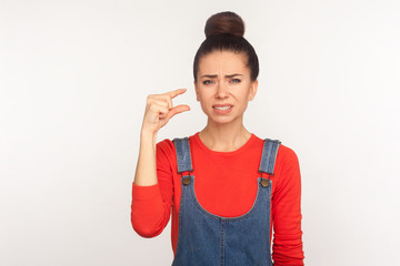 Too small! Portrait of dissatisfied girl with hair bun in denim overalls showing a little bit...