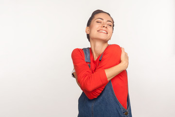 Positive self-esteem. Portrait of stylish girl embracing herself and smiling with expression of pleasure, being selfish and narcissistic admiring her appearance. indoor studio shot, white background