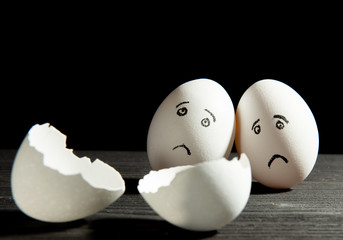 two sad eggs look at a broken egg on a black background