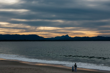 Mother with daughter on an empty beach at sunset with mountains in the background 