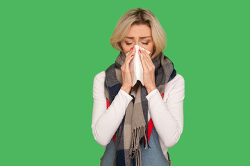 Runny nose, flu symptoms. Portrait of sick adult woman wrapped in warm scarf sneezing and blowing...