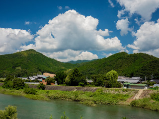 Fototapeta na wymiar 青い空と白い雲と川と山のある日本の里山の風景。