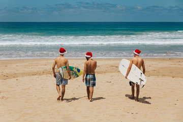 Three guys walking to the beach with surfboards and Santa hats © Lennart