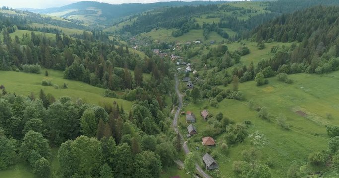 Panoramic view of Ukraine village and green forest of Carpathian Mountains in the spring. Field, white sky and beautiful green valley. Drone view from High Mountain Range. 4K video.