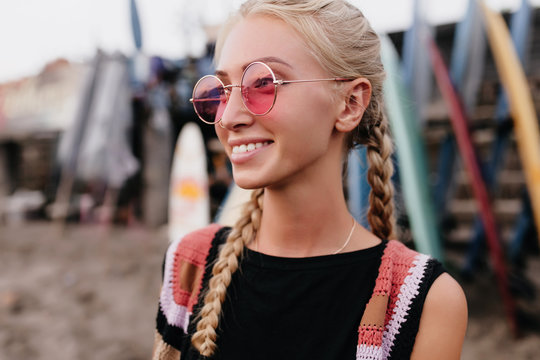 Romantic girl with trendy hairstyle posing in pink sunglasses. Outdoor shot of gorgeous blonde lady with braids enjoying good weather.