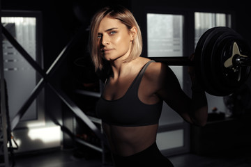 Fototapeta na wymiar Athletic young blonde woman doing heavy barbell exercise in fitness class.