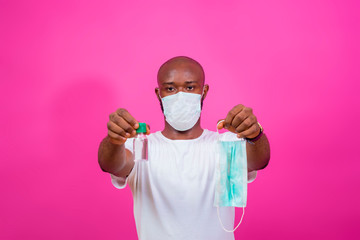 young black man wearing a nose mask and holding out a nose mask and a hand sanitizer