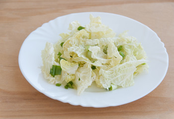 Fresh salad of green onion and chinese cabbage leaves on a white dish. Wooden table. Close-up