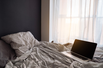 Front view of laptop computer with blank screen on bed with сup of tea at morning.