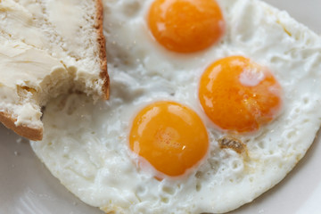 Three fried eggs and bread and butter on a plate.