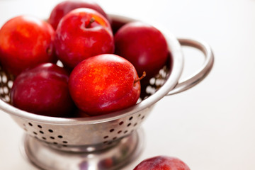 Red plums in colander. White background.