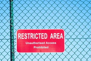 Restricted Area warning sign hanging on chain link fence outdoors against bright blue sky