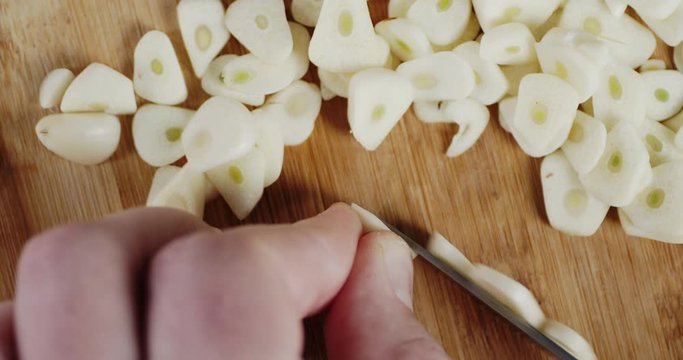Male hands slicing peeled cloves of garlic into pieces.
