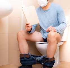 man sitting in bathroom with face mask reading a book isolation covid-19