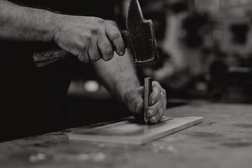 Les mains d'un artisan et son marteau dans son atelier