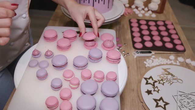 Woman is making macarons and putting them on a table. There are macarons of different size.
