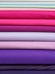 Bright pink and purple fabric laid in layers, close-up. Background with a bright and expressive fabric texture. Assortment of multi-colored fabrics in the store