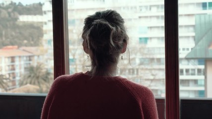 Girl looking out the window while locked up at home during confinement due to coronavirus