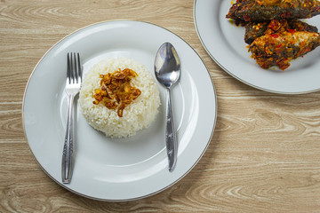 Nasi putih or white rice in white plate served with ikan balado on wooden background. top view