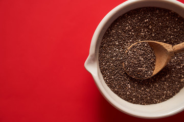 wooden spoon with chia seeds lies in a white mortar on a red background closeup banner