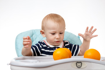 Cheerful little boy is eating oranges on a white background