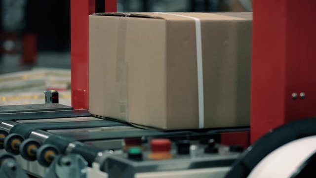 Parcels in a warehouse with cardboard box moving along the packaging line. Plastic straps are attached with a strapping machine on the package. Automation of online shipping logistics