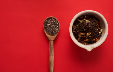 tea leaves with slices of fruit in a white bowl and a wooden spoon on a red background top view