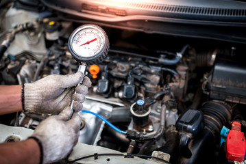 The auto mechanic is about to measure compression in the cylinder of a car engine using a...