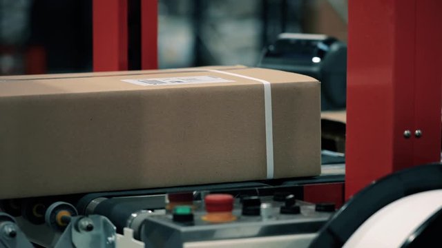 Parcels in a warehouse with cardboard box moving along the packaging line. Plastic straps are attached with a strapping machine on the package. Automation of online shipping logistics