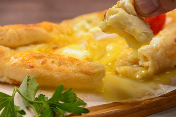 Ajarian traditional khachapuri with egg. Tomato and greens in the background.