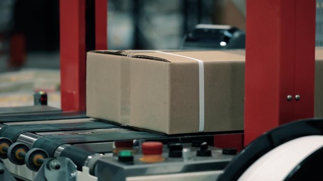 Parcels in a warehouse move along and wait in line the packaging line. Plastic straps are attached with a strapping machine on the package. Automation of online shipping logistics