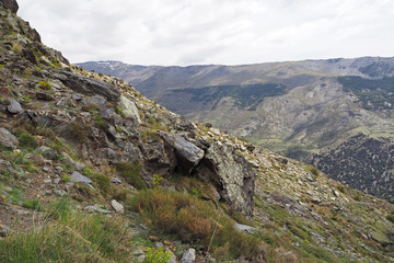 The mountain landscape with the slope covered by green grass, the grey glance rocks, the cloudy sky on the sunny spring day.