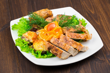 mix of chicken meat with leaves of greens, dill, cheese and a slice of orange in a square white plate on a wooden table