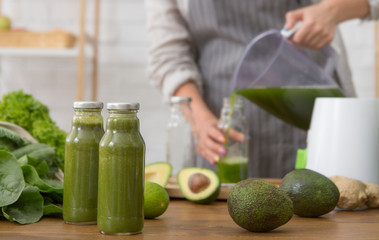 Woman in linen apron pouring green detox smoothie into bottle