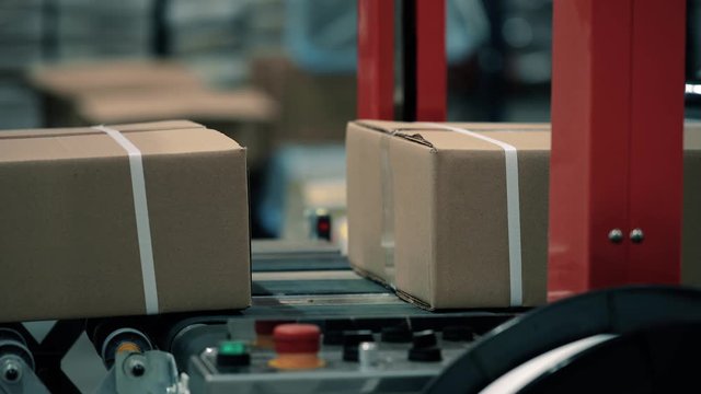 Parcels in a warehouse move along and wait in line the packaging line. Plastic straps are attached with a strapping machine on the package. Automation of online shipping logistics