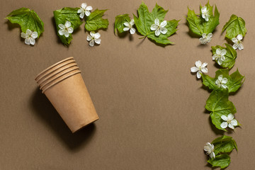 disposable paper cups on a brown background. frame of green leaves and cherry flowers. environmentally friendly. place for text