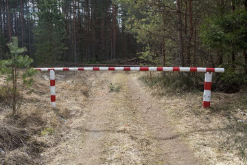 Fototapeta na wymiar The barrier closes the road to the forest. The barrier is red and white. Ban on visiting the forest. Fire hazard period. Forest protection from fires.