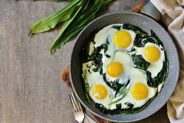 fried eggs with wild garlic as a shakshuka. fried eggs in a frying pan under gray marble on a table, top view. Keto diet dish