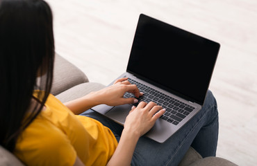 Working or studying online. Young girl using laptop with blank screen at home, space for your design