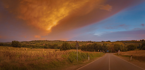 Breathtaking wide angle view of the beautiful sunset over the road with the storm front and orange clouds in Tuscany, Italy