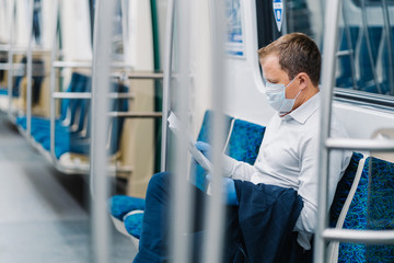 Social distance. Coronavirus quarantine. Businessman travels in underground, sits and reads newspaper, wears medical mask and gloves, prevents himeself in public transport. Pandemic Covid-19