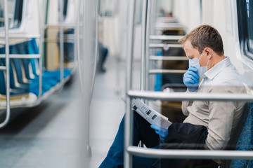 Prohibition of free movement. Man in formal clothes, coughs and has symptoms of coronavirus, wears protective medical mask and gloves, reads newspaper, poses in subway or metro, commutes to work