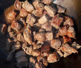 The meat is fried in oil on a cast-iron cauldron.