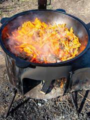 Carrots are fried in oil on a cast-iron cauldron.