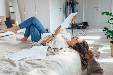A young woman is lying on a bed in the bedroom reading