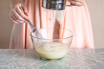 A woman sifts flour into a bowl, the process of kneading the dough.