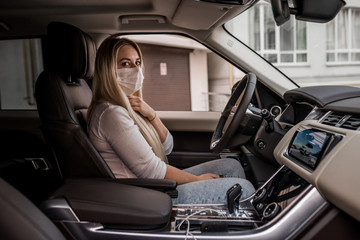 Obraz na płótnie Canvas girl in a medical mask. beautiful blonde driving an expensive car. coronavirus, disease, infection, quarantine, medical mask, covid-19