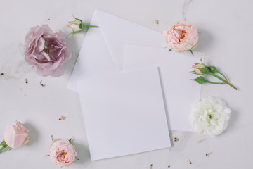 Elegant floral composition with envelope, empty white paper blank on marble background.  Wedding...