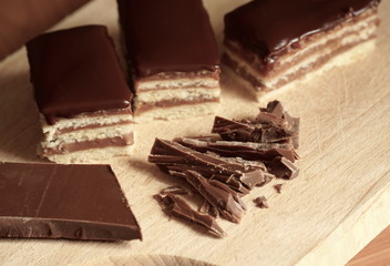 Chocolate layer cake and pieces of grated chocolate served on the wooden kitchen board